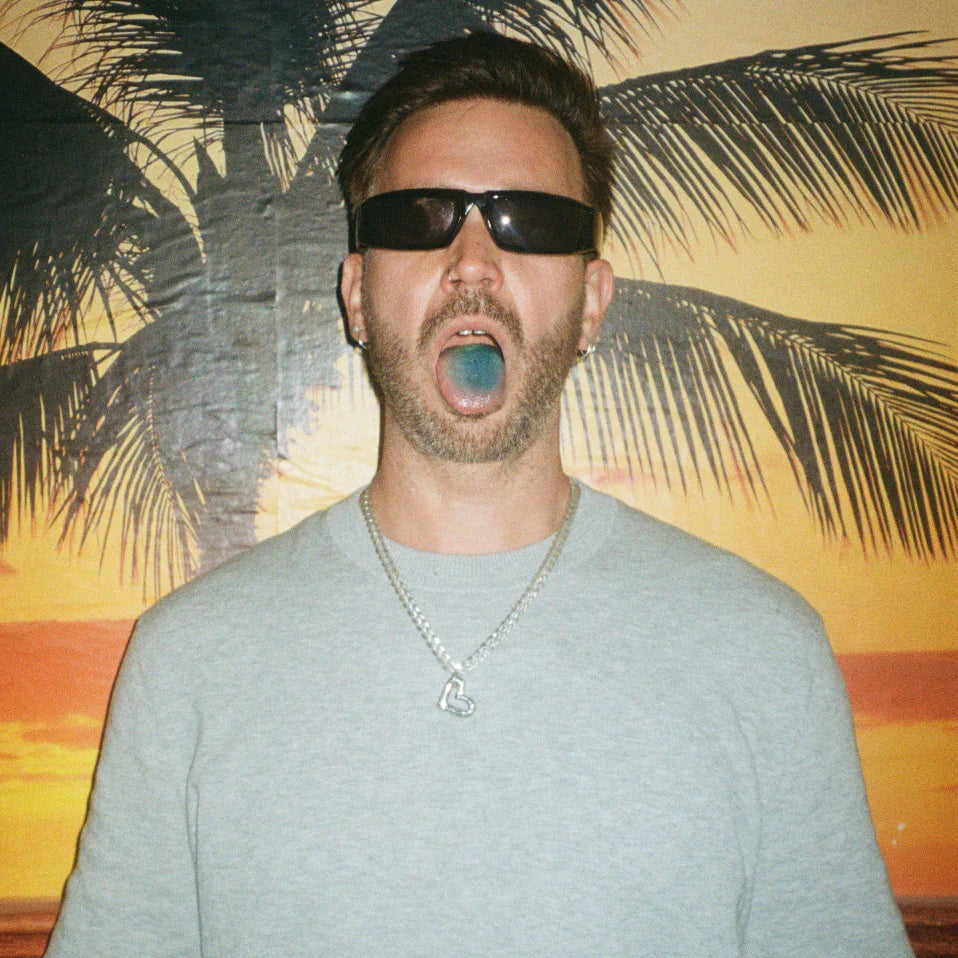 Mann mit Sonnenbrille und silberner Halskette vor Palmen-Hintergrund, blaue Zunge
