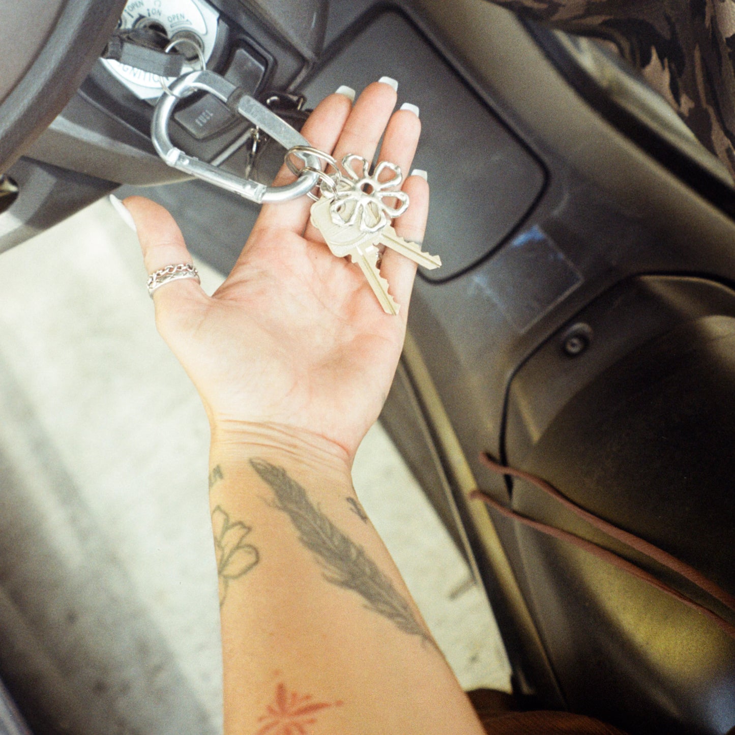 Schlüsselbund mit auffälligem, blumenförmigem Chunky-Charm-Anhänger in Hand im Auto