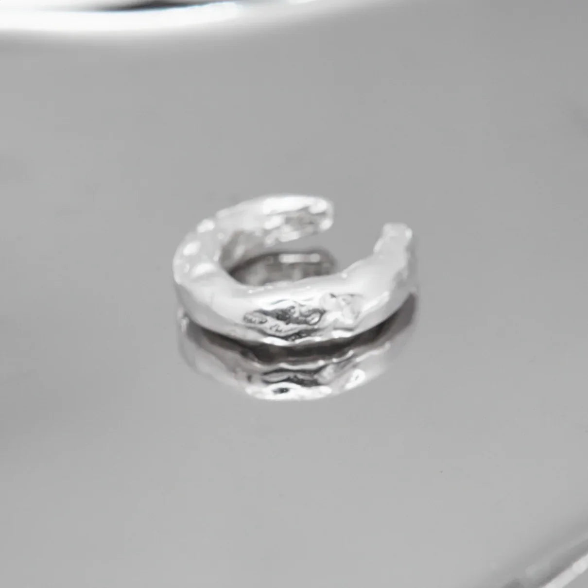 Handgefertigter Ear Cuff aus 925er Silber mit organischer Struktur auf spiegelnder Oberfläche